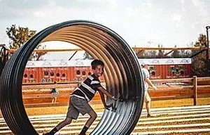 10_original Child playing inside a large metal wheel outdoors on a sunny day.