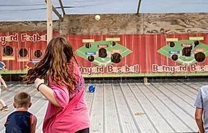 16_original Children and woman playing barnyard-themed target throwing game indoors.