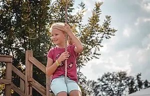 6_original Child holding onto a rope swing outdoors with trees in the background.
