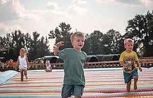 8_original Children playing on a large padded outdoor surface with trees in the background.