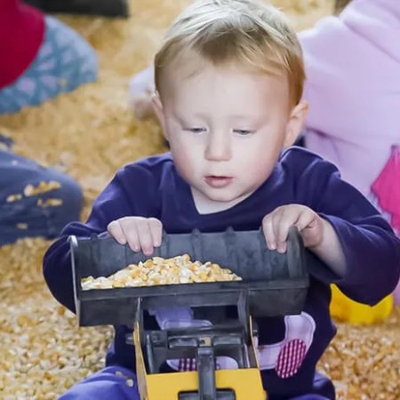 Child playing with toy loader on corn kernels indoors.