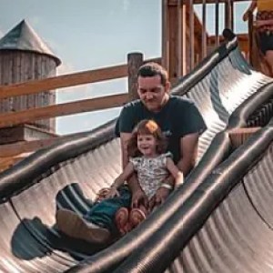 Adult and child sliding down a playground slide together with a silo in the background.
