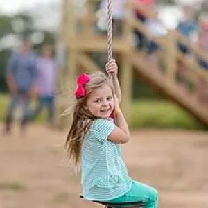 Smiling girl with red bow swinging on a rope in a park.