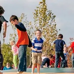 Children playing on a colorful outdoor bouncy surface with trees in background.