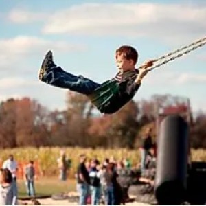 Child swinging on a rope swing at an outdoor event with people in the background.